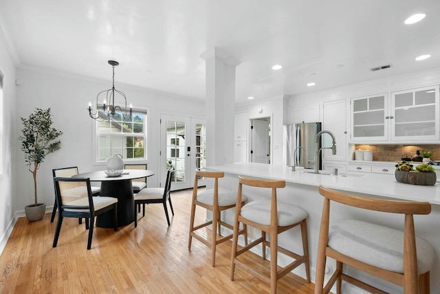 kitchen featuring glass insert cabinets, a kitchen bar, white cabinets, visible vents, and freestanding refrigerator