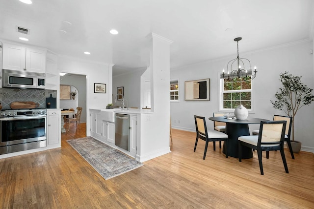 kitchen with stainless steel appliances, light countertops, visible vents, light wood-style floors, and crown molding