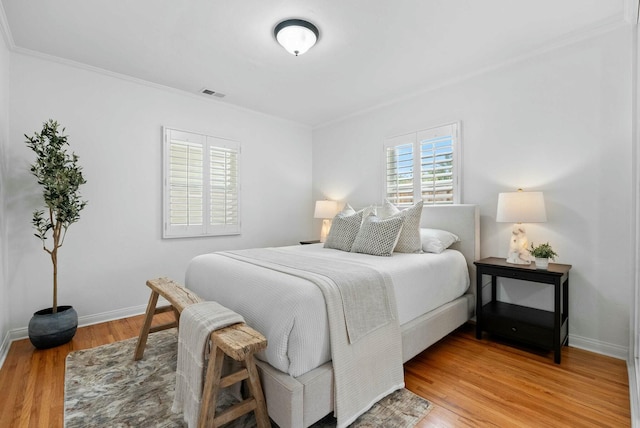 bedroom with light wood-style flooring, visible vents, crown molding, and baseboards