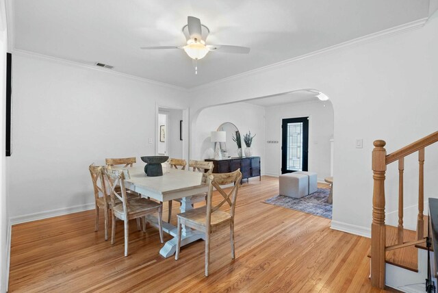 dining space featuring light wood finished floors, arched walkways, baseboards, visible vents, and ceiling fan