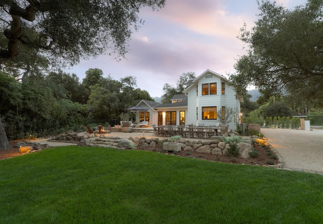 back of house at dusk featuring a patio and a yard