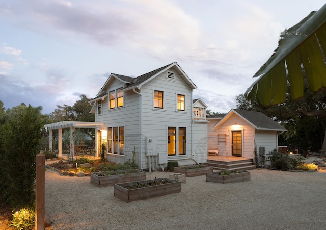rear view of property featuring an outdoor structure, a pergola, and a vegetable garden