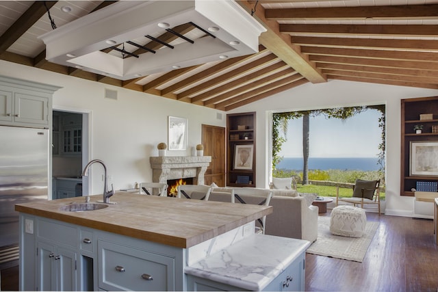 kitchen with stainless steel fridge, a sink, wood counters, open floor plan, and a center island with sink