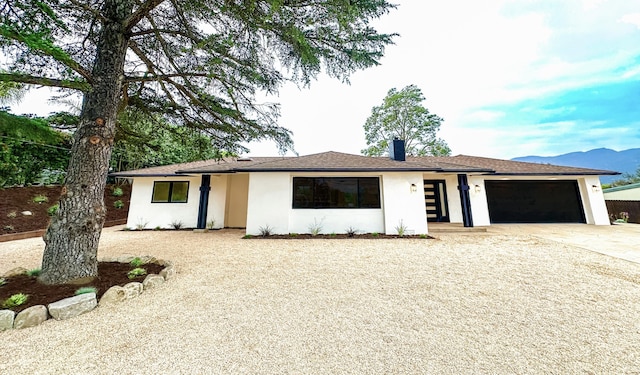 ranch-style home with concrete driveway, a chimney, a garage, stucco siding, and roof with shingles