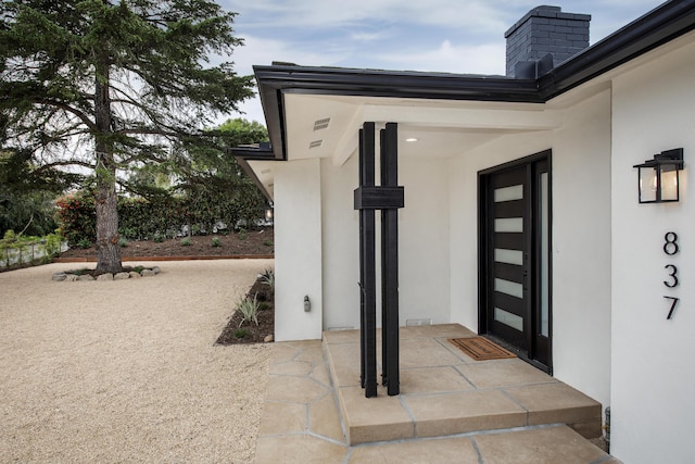 view of exterior entry with stucco siding and a chimney