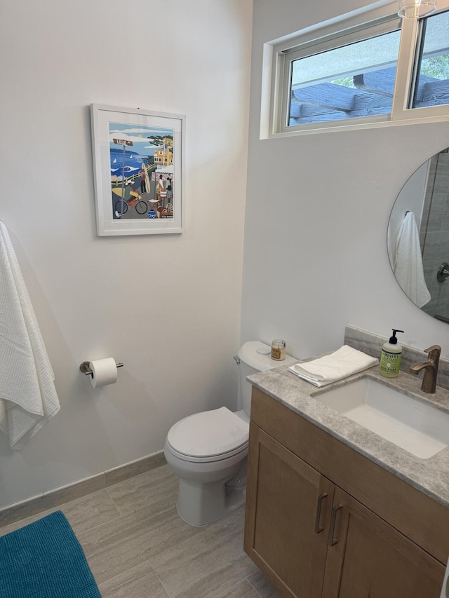 bathroom with baseboards, a healthy amount of sunlight, toilet, and vanity