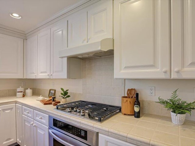 kitchen featuring under cabinet range hood, tile counters, stainless steel appliances, and white cabinetry