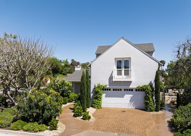 view of front of home featuring decorative driveway, a balcony, an attached garage, stucco siding, and roof with shingles