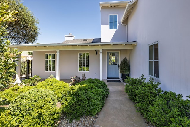 doorway to property with stucco siding, fence, and a chimney