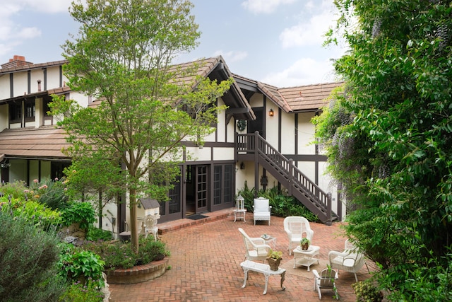 rear view of house with a tiled roof, french doors, a patio, stucco siding, and stairs