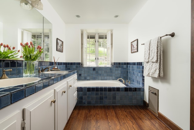 full bathroom featuring a relaxing tiled tub, wood finished floors, a sink, and double vanity