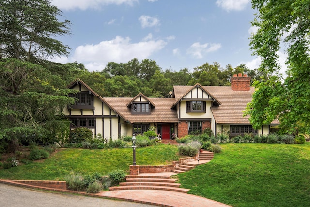 english style home with a front lawn, a chimney, and stucco siding
