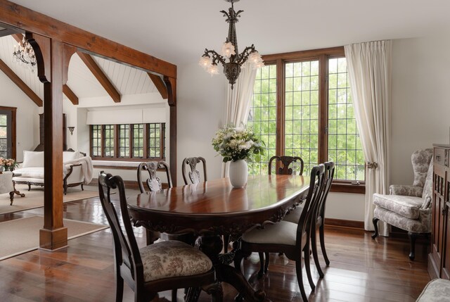 dining space with lofted ceiling with beams, an inviting chandelier, dark wood-type flooring, and baseboards