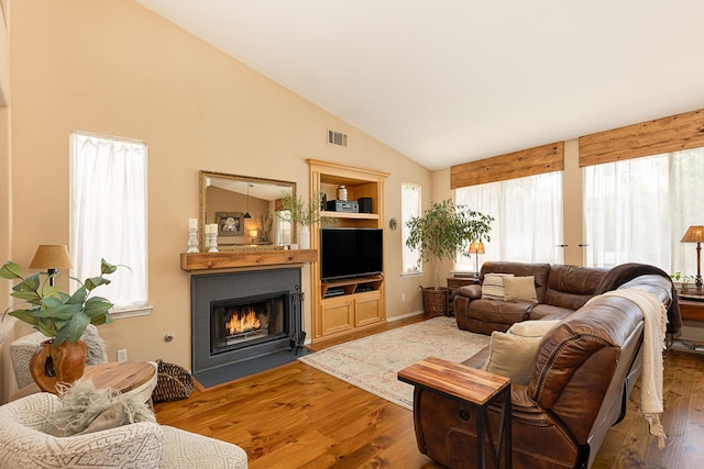 living room featuring a fireplace with flush hearth, wood finished floors, visible vents, and high vaulted ceiling