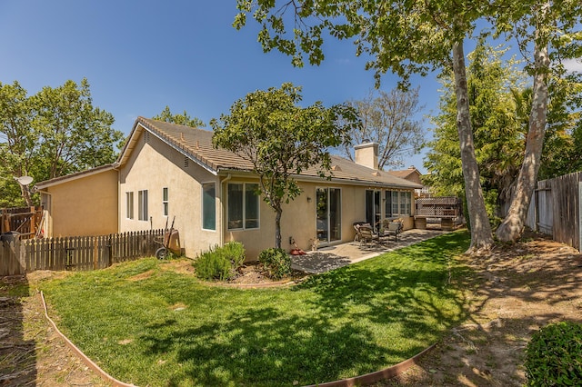 rear view of house featuring a patio area, a yard, a fenced backyard, a chimney, and stucco siding