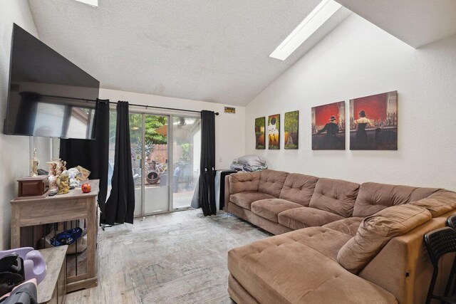 living area featuring high vaulted ceiling, light wood-style flooring, a textured ceiling, and a skylight