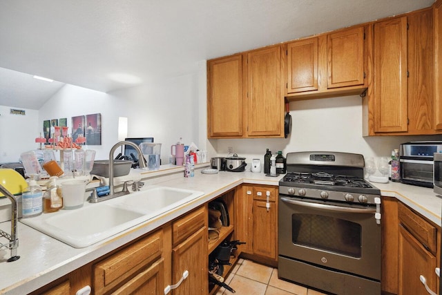 kitchen featuring a sink, brown cabinetry, light tile patterned floors, light countertops, and stainless steel range with gas stovetop