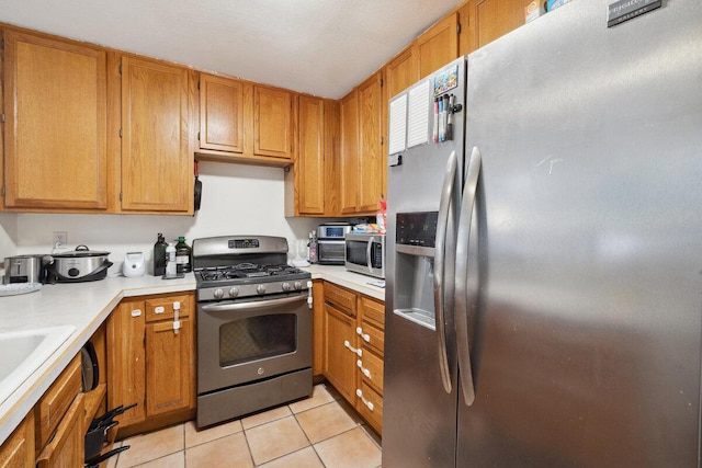 kitchen featuring brown cabinetry, light tile patterned flooring, stainless steel appliances, and light countertops