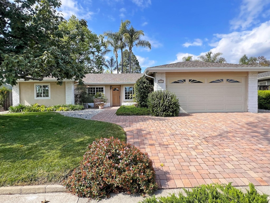 single story home featuring decorative driveway, a front yard, and an attached garage