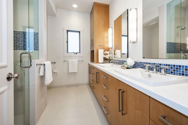 bathroom with double vanity, a shower stall, baseboards, and a sink