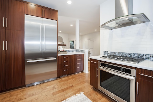 kitchen with exhaust hood, backsplash, appliances with stainless steel finishes, and light countertops