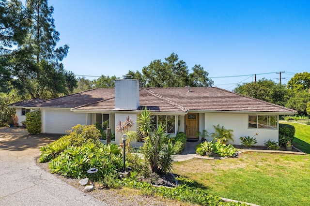 ranch-style house featuring a garage, a front yard, stucco siding, a chimney, and driveway