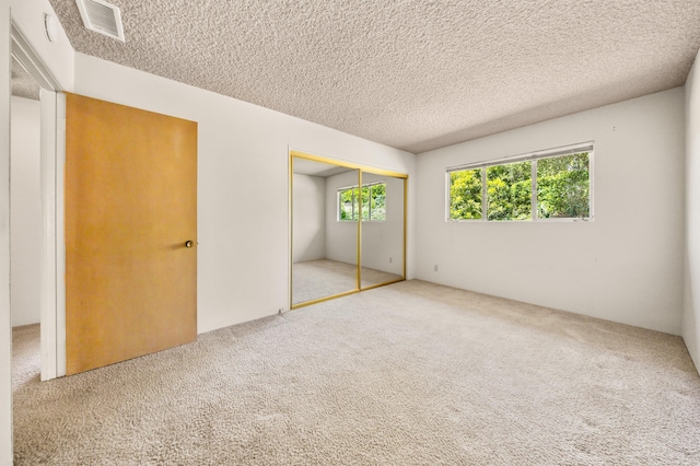 unfurnished bedroom featuring carpet, a closet, a textured ceiling, and visible vents