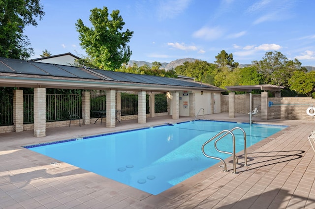 community pool featuring a mountain view, a patio area, and fence