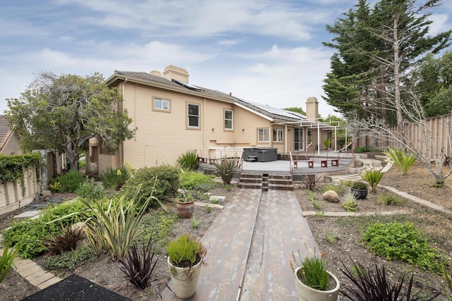 back of property featuring a wooden deck, solar panels, a fenced backyard, and a chimney