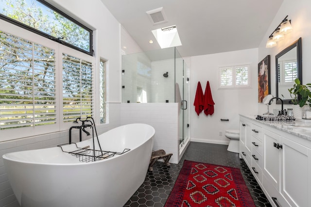 bathroom with a freestanding bath, a shower stall, toilet, vanity, and lofted ceiling with skylight