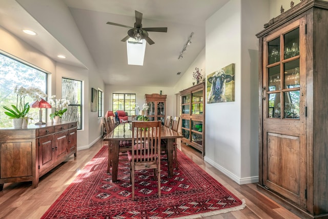 dining room with vaulted ceiling with skylight, rail lighting, light wood finished floors, baseboards, and a ceiling fan