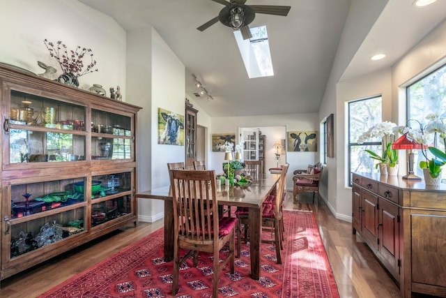 dining room featuring vaulted ceiling with skylight, a ceiling fan, track lighting, baseboards, and wood finished floors