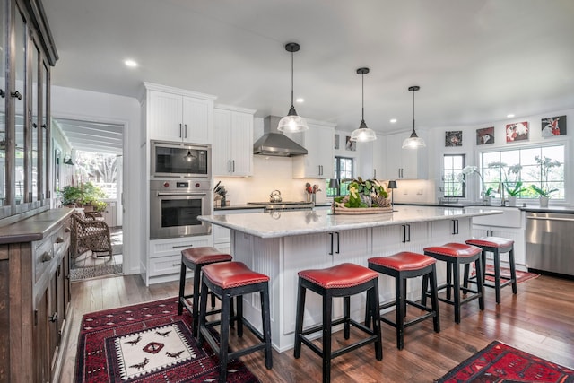 kitchen featuring appliances with stainless steel finishes, wall chimney range hood, white cabinets, a center island, and a kitchen breakfast bar