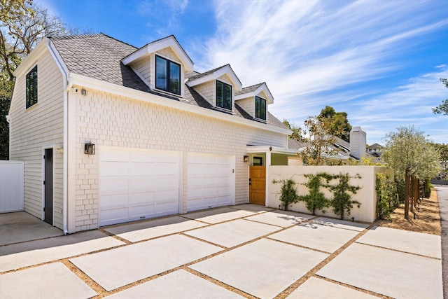 view of property exterior with concrete driveway, roof with shingles, a garage, and fence