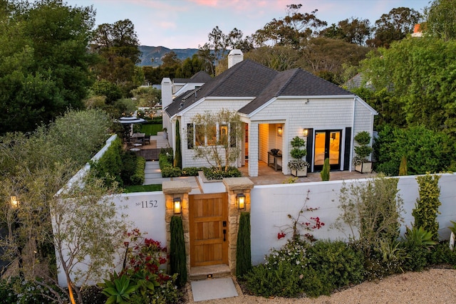 view of front of property with a wooden deck, a fenced front yard, a gate, a chimney, and french doors