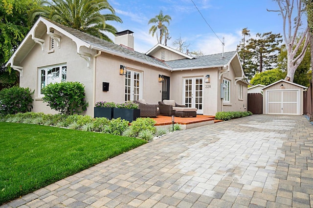view of front of property featuring a garage, a storage shed, a chimney, decorative driveway, and french doors