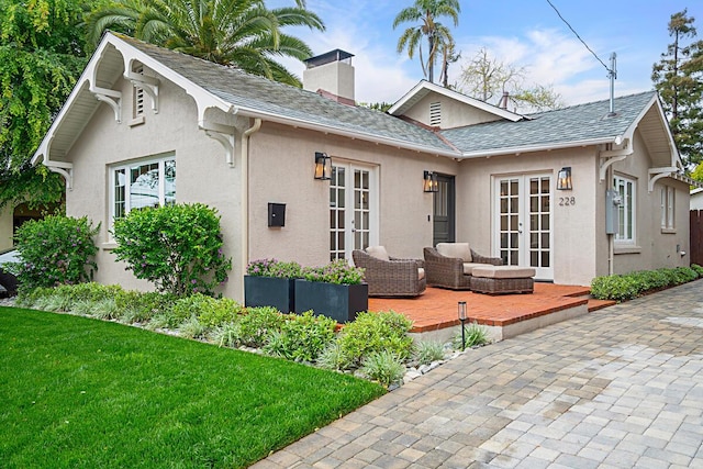 rear view of property with stucco siding, a chimney, french doors, a patio, and a lawn