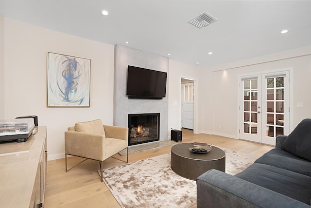 living area with visible vents, light wood-style floors, a fireplace, and french doors