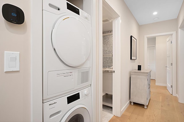 laundry room with recessed lighting, baseboards, stacked washer and dryer, and light wood-style flooring