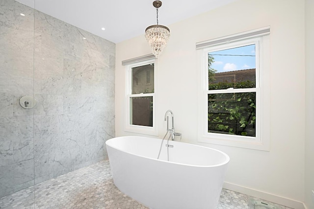 bathroom with baseboards, a freestanding bath, a notable chandelier, and a tile shower