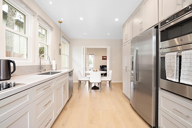 kitchen with a sink, light countertops, baseboards, stainless steel appliances, and light wood-style flooring