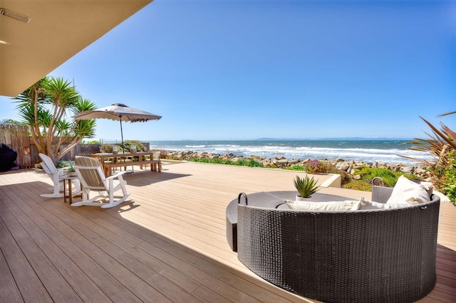 wooden terrace featuring a water view, a view of the beach, and outdoor dining area