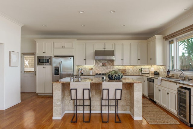 kitchen with beverage cooler, under cabinet range hood, light stone countertops, and stainless steel appliances