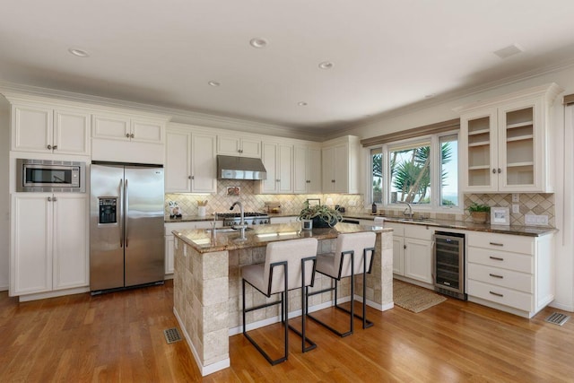kitchen featuring appliances with stainless steel finishes, wood finished floors, tasteful backsplash, under cabinet range hood, and wine cooler