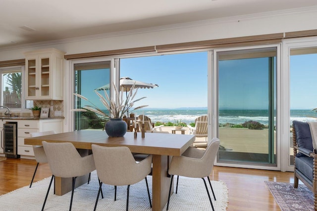 dining room featuring crown molding, a water view, light wood-type flooring, and wine cooler