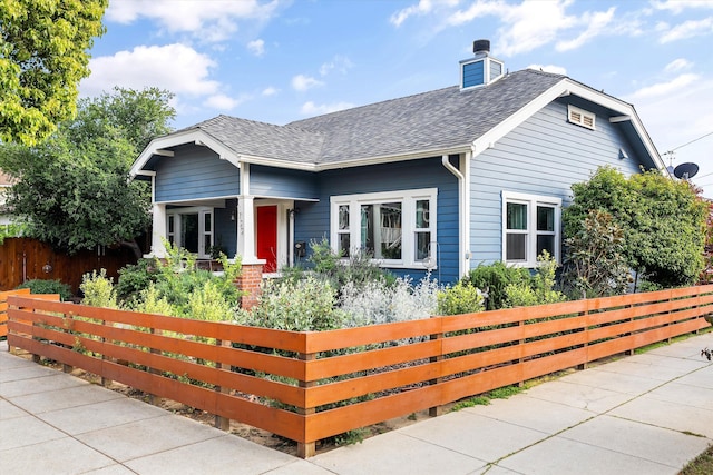 view of front of house with covered porch, a chimney, fence private yard, and roof with shingles