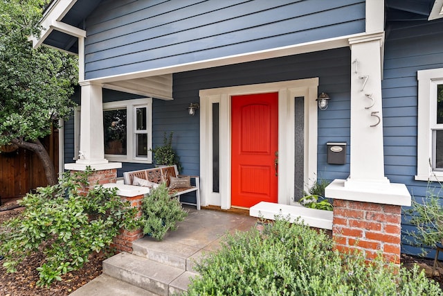 view of exterior entry featuring fence and covered porch