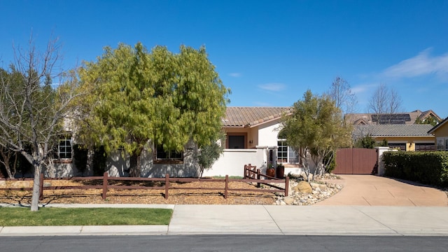 view of property hidden behind natural elements featuring a tiled roof, concrete driveway, a fenced front yard, and stucco siding
