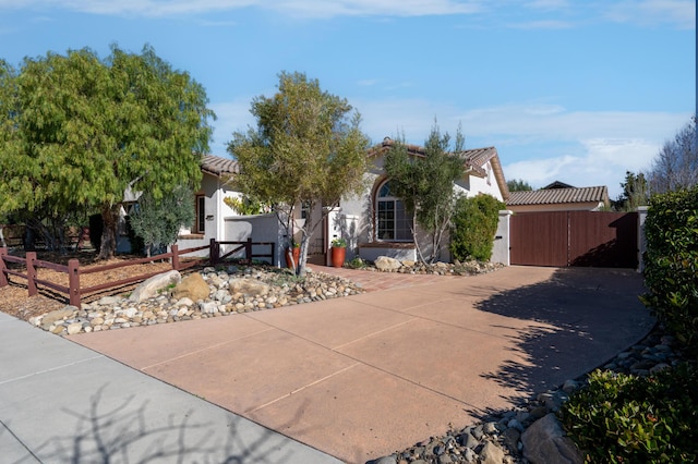 view of property hidden behind natural elements featuring a gate, a fenced front yard, stucco siding, and a tiled roof