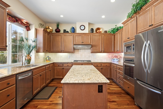 kitchen featuring dark wood-style floors, a center island, under cabinet range hood, a sink, and stainless steel appliances